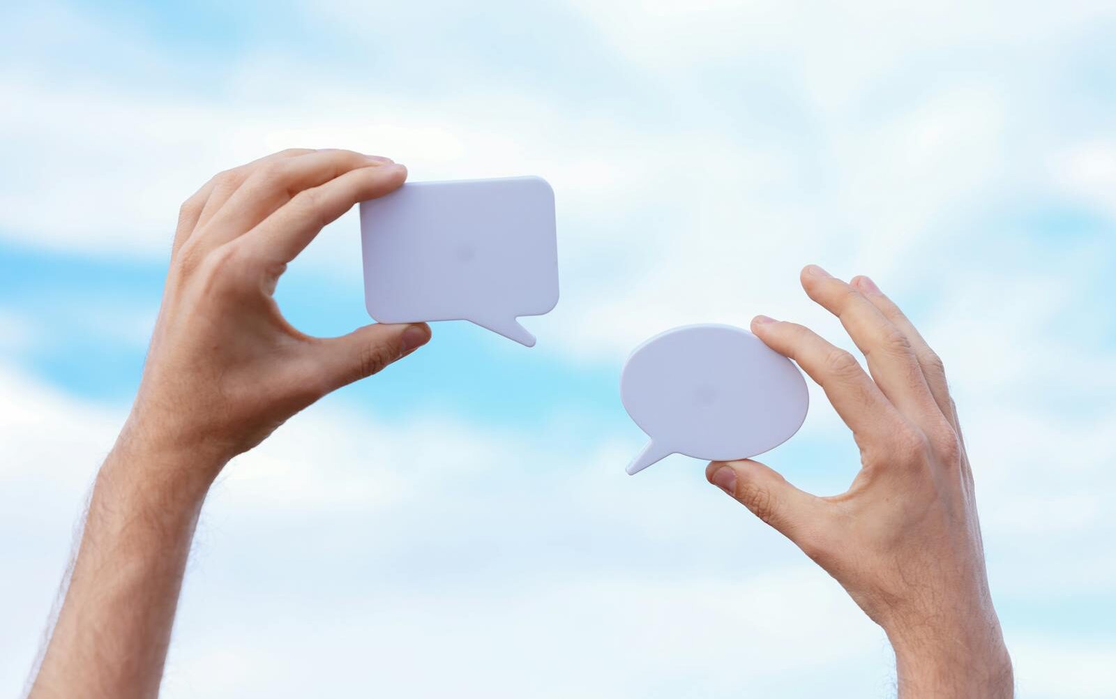 Close-up of hands holding speech bubbles, symbolizing communication and dialogue against a blue sky.